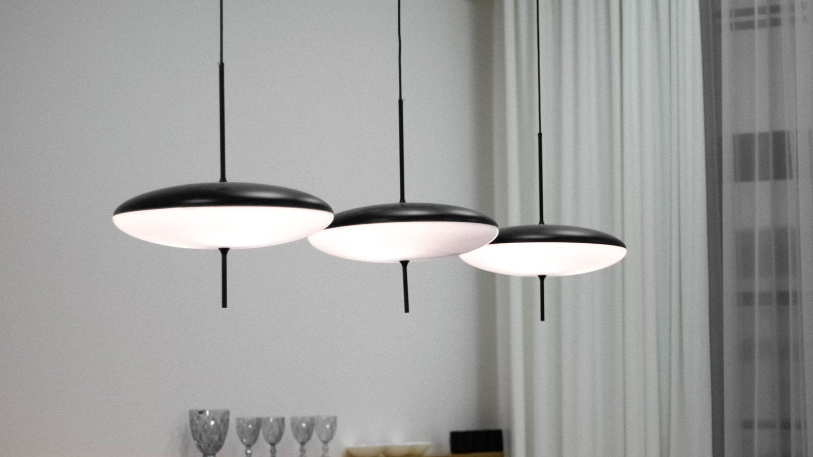 Trzy czarne lampy wiszące z płaskimi kloszami nad długim drewnianym stołem jadalnym w jasnym wnętrzu